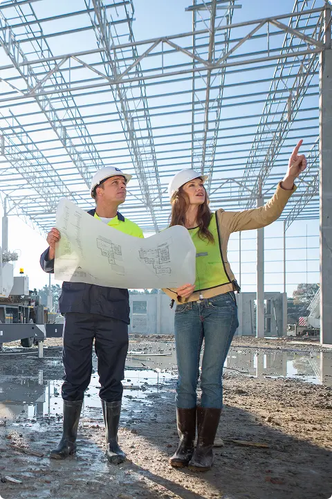 une entreprise à taille humaine avec une expertise de haut niveau Architectes discutant d'un plan sur chantier de construction.